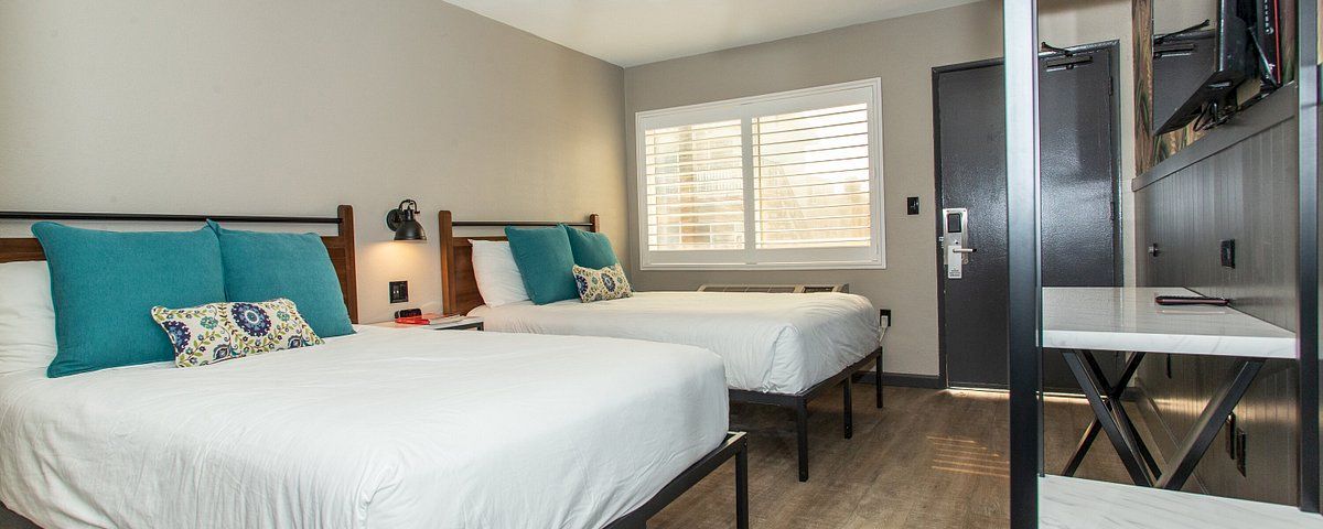 A hotel room with two beds, a desk, and a window.