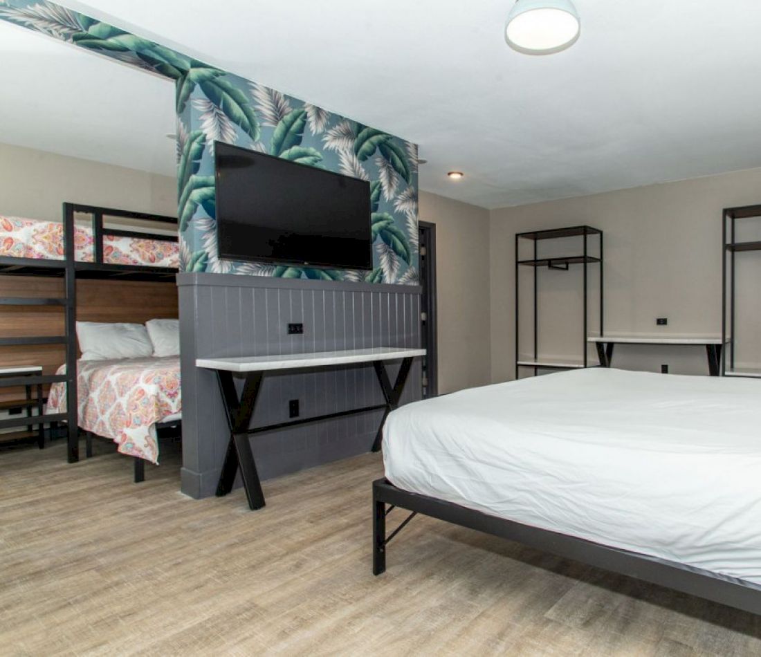 A wide view of a hotel room with bunk beds, a single bed, a TV, and a desk.