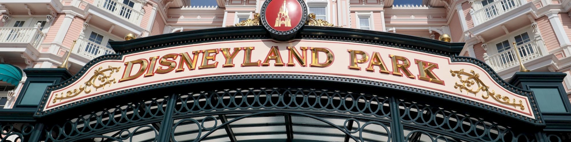 This image shows the entrance of Disneyland Park, featuring an ornate sign with a clock and decorative architecture in the background.