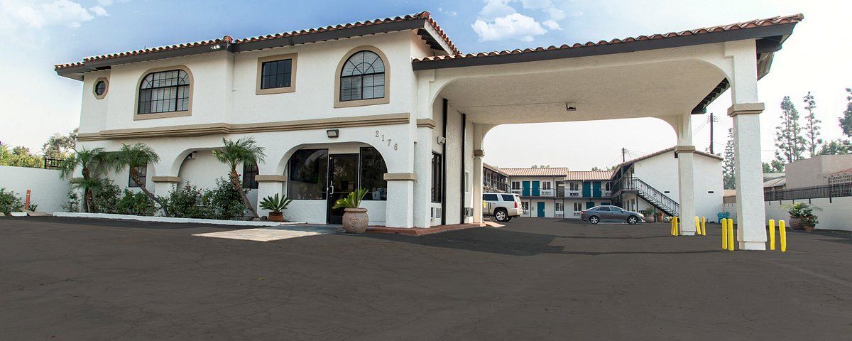 A white stucco building with a clay tile roof and arched entryway, with a covered parking area and columns.