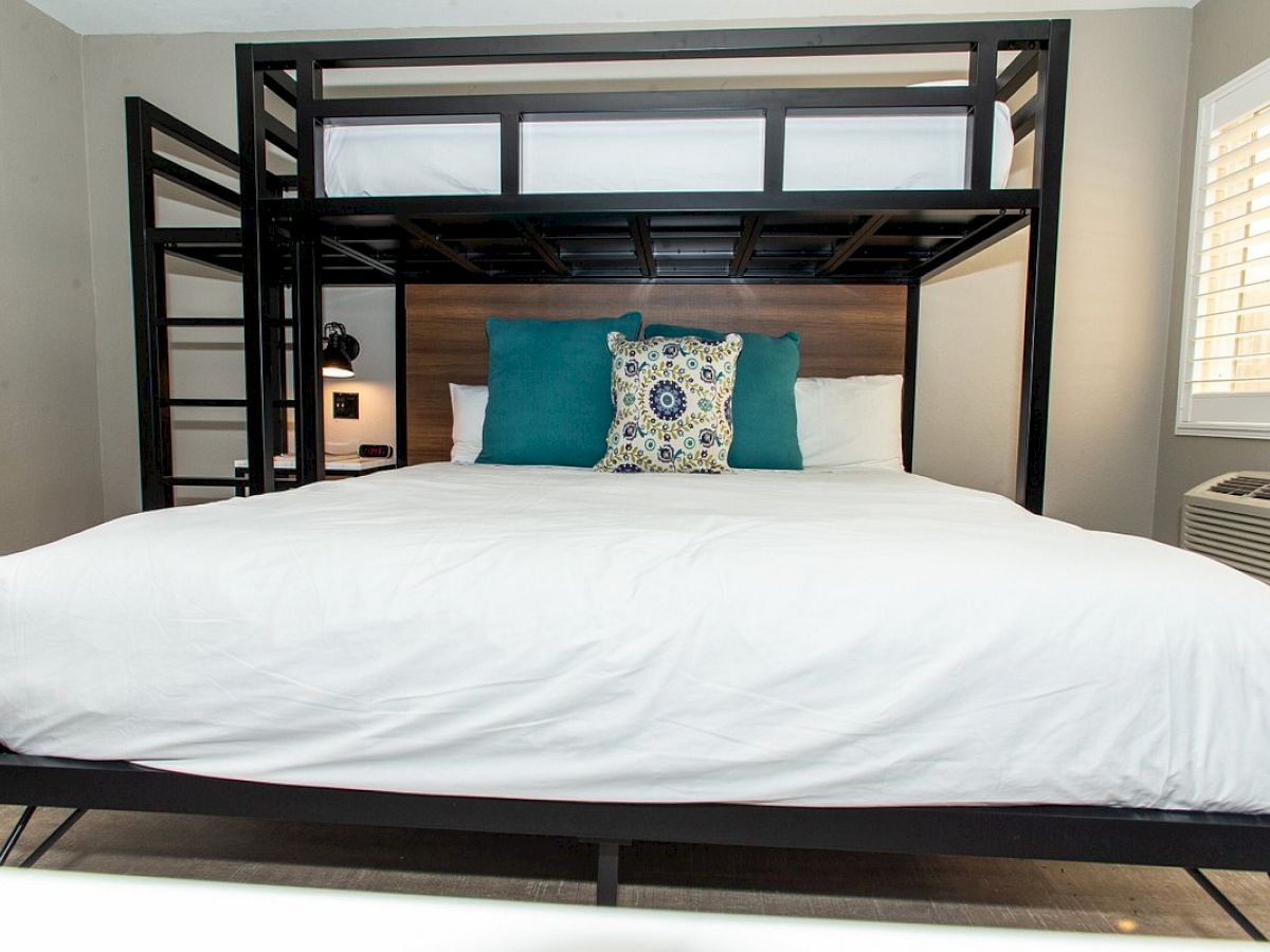 The image shows a bedroom with a bunk bed setup. The lower bed is a king-sized bed with two teal pillows and one patterned pillow.