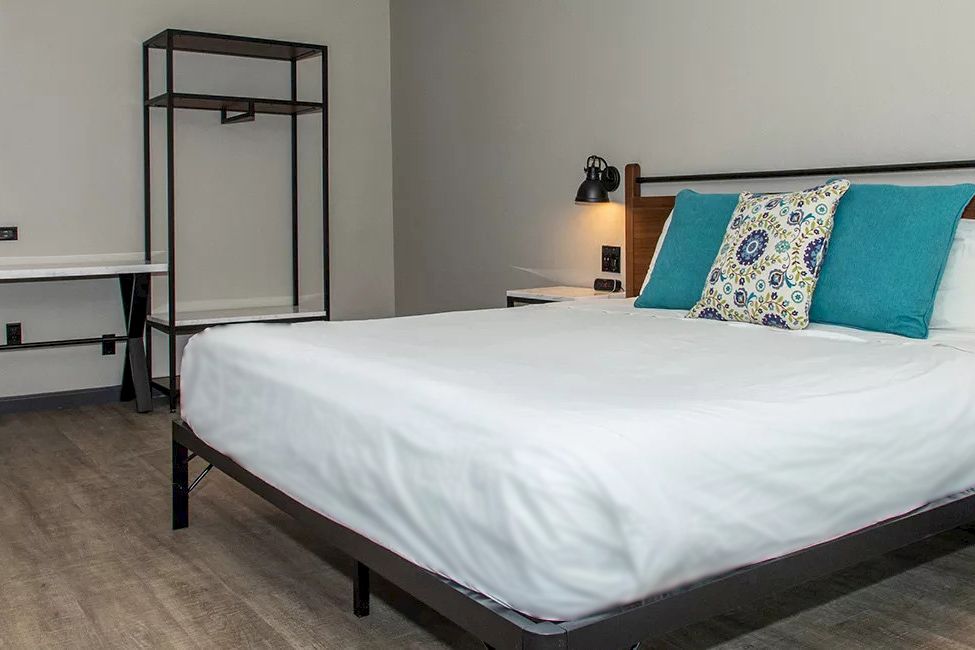 A neatly made bed with white sheets and blue pillows in a room with a desk and a rack.