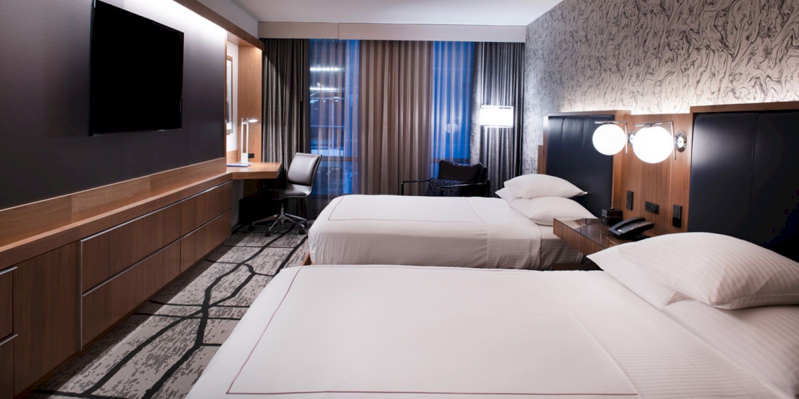 This image depicts a modern hotel room with two neatly made beds, a work desk, a flat-screen TV, and stylish decor.