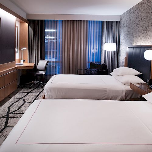 A modern hotel room with two double beds, a wall-mounted TV, a desk with a chair, bedside tables, and stylish lighting and decor ending the sentence.