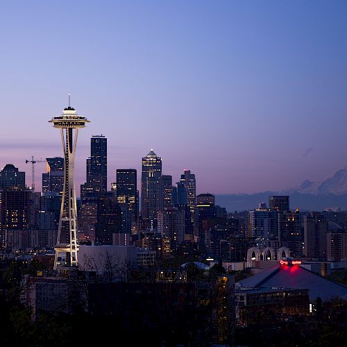 This image shows a city skyline at dusk with recognizable landmarks including a tower and a distant mountain together.