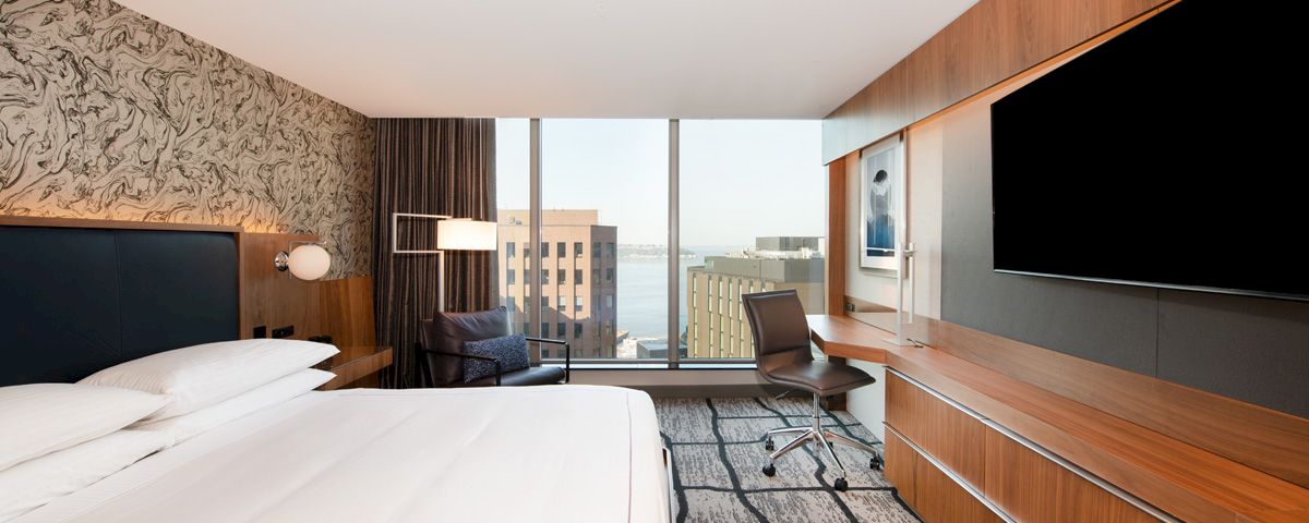 A hotel room with a bed, desk, TV, and window