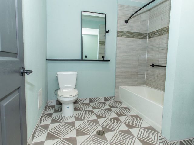 A clean and modern bathroom with a toilet, shower, bathtub, and mirror.