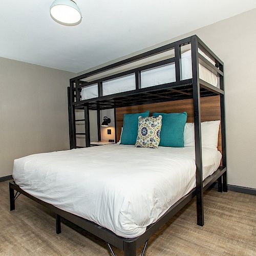 A modern bedroom with a bunk bed featuring a double bed below and a single bed above, equipped with stylish pillows and a wooden floor finish.