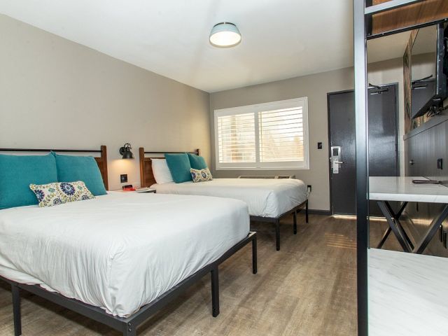 A hotel room with two beds, a window, a desk, and a TV.
