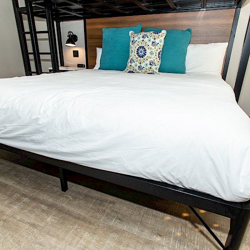 A neatly made bed with white linens, a wooden headboard, and two turquoise pillows along with a decorative pillow in the center.