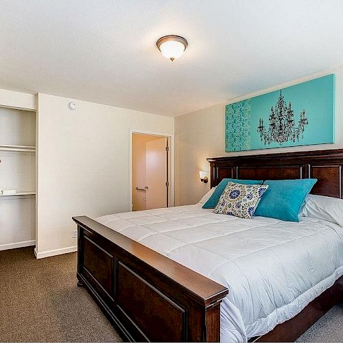 A tidy bedroom with a large bed, turquoise accents, wall art, a flat-screen TV, open closet, luggage rack, and nightstands with lamps, ending the sentence.