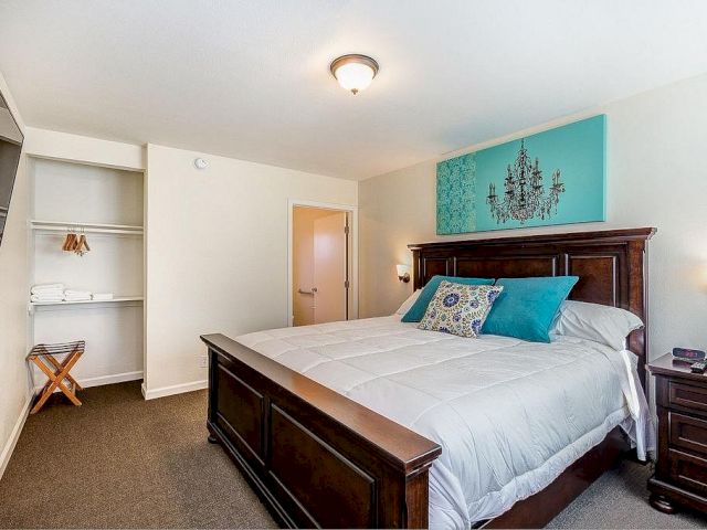 A wide view of a guest room with a large bed, nightstand, closet, and artwork.