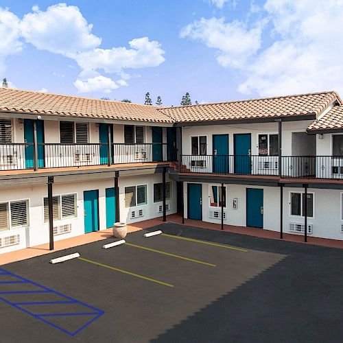 The image depicts the exterior of a two-story motel with a central parking lot and blue doors to each room.