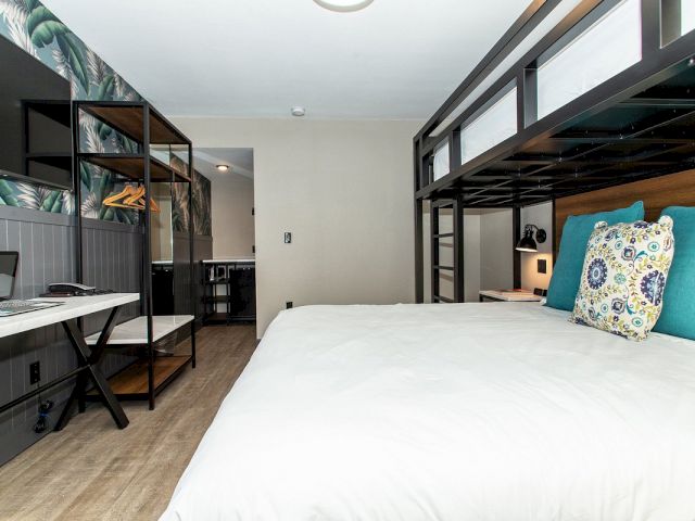 A wide view of a hotel room with a bunk bed, desk, and TV.
