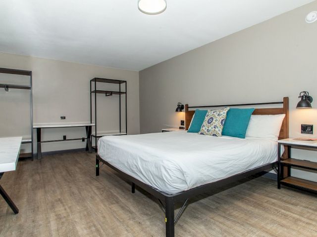 A wide view of a guest room with a bed, desk, nightstand, and closet.