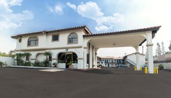 The image shows a two-story building with an arched entrance and a covered driveway, likely a hotel or motel, against a clear sky.