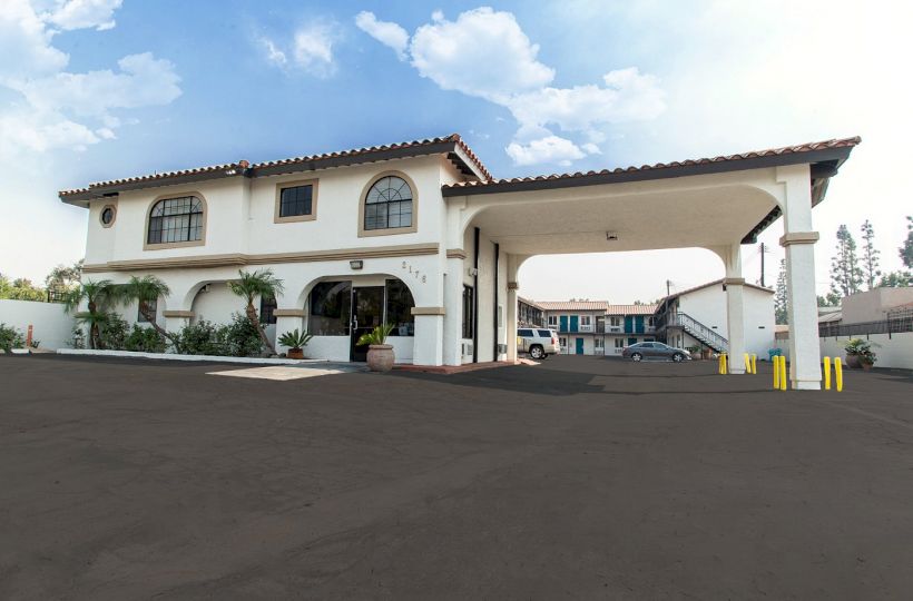 The image shows a two-story building with an arched entrance and a covered driveway, likely a hotel or motel, against a clear sky.