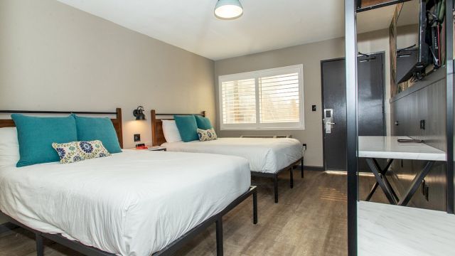 A hotel room with two beds, a desk, and a TV