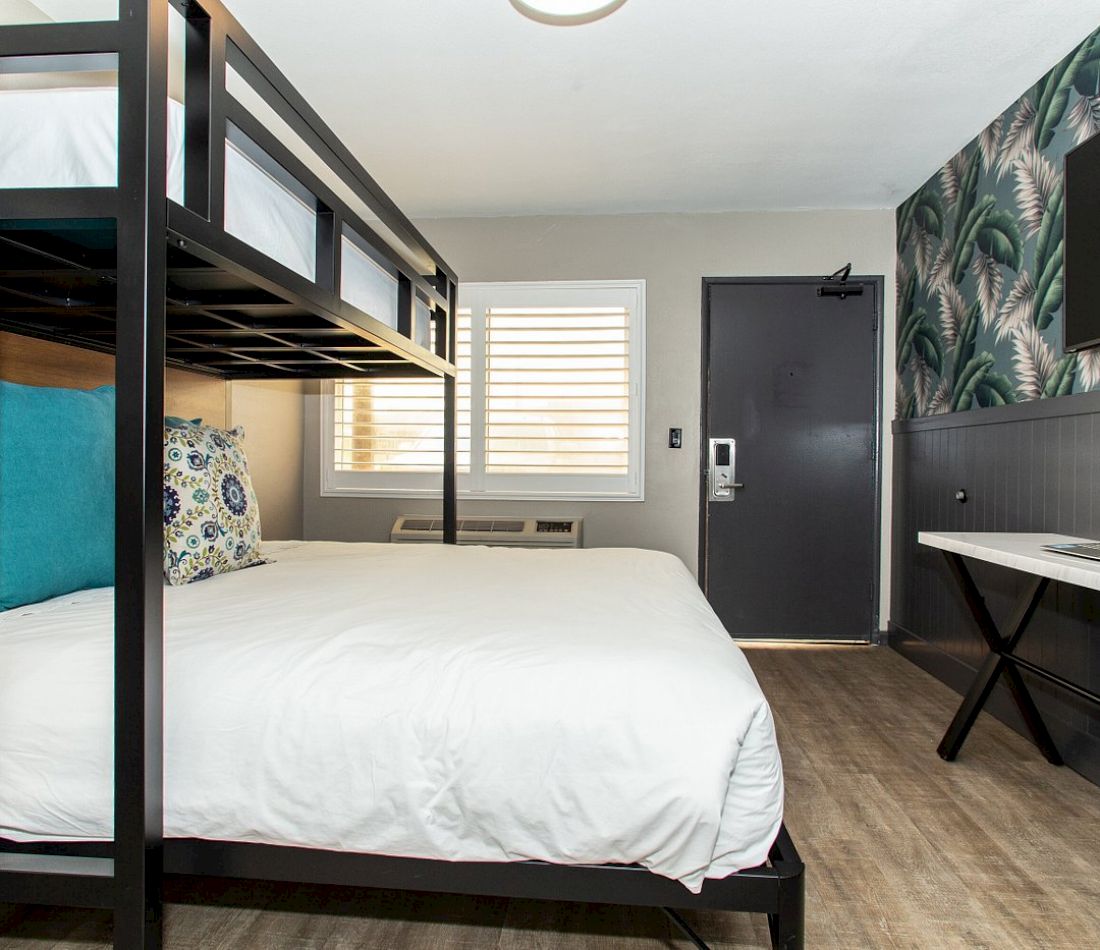 A hotel room with a bunk bed, desk, TV, window, and door.